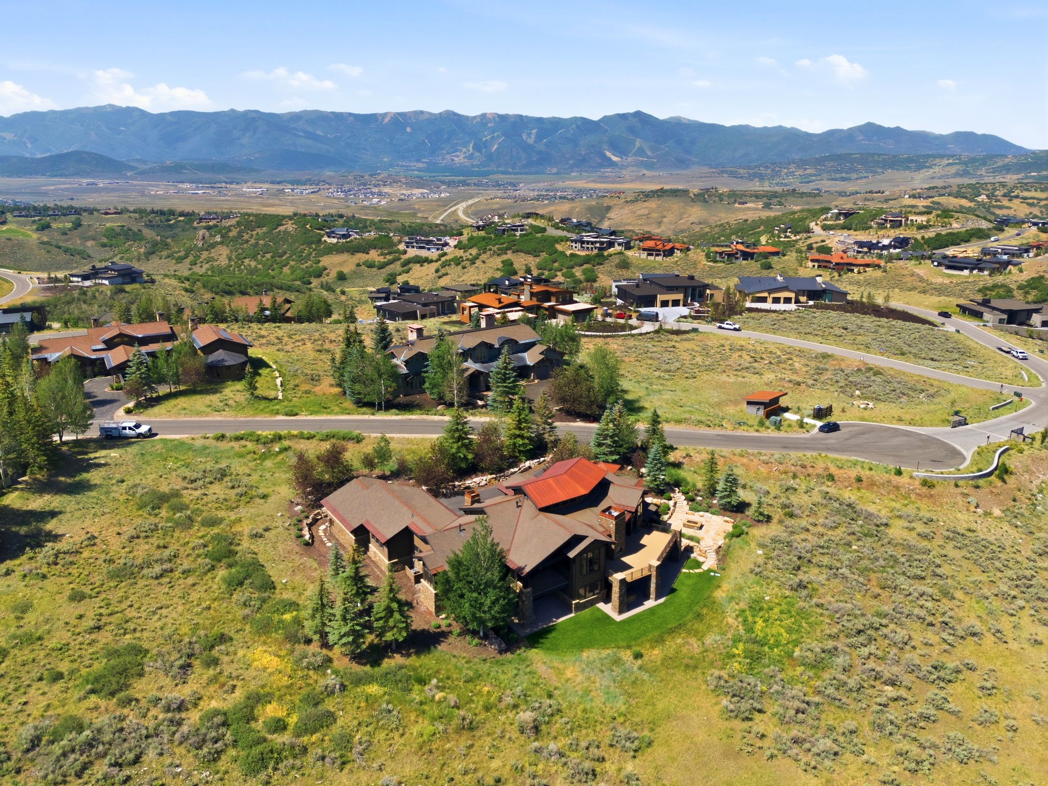 Expansive mountain property featuring a multi-level residence with a prominent red roof and a stone patio