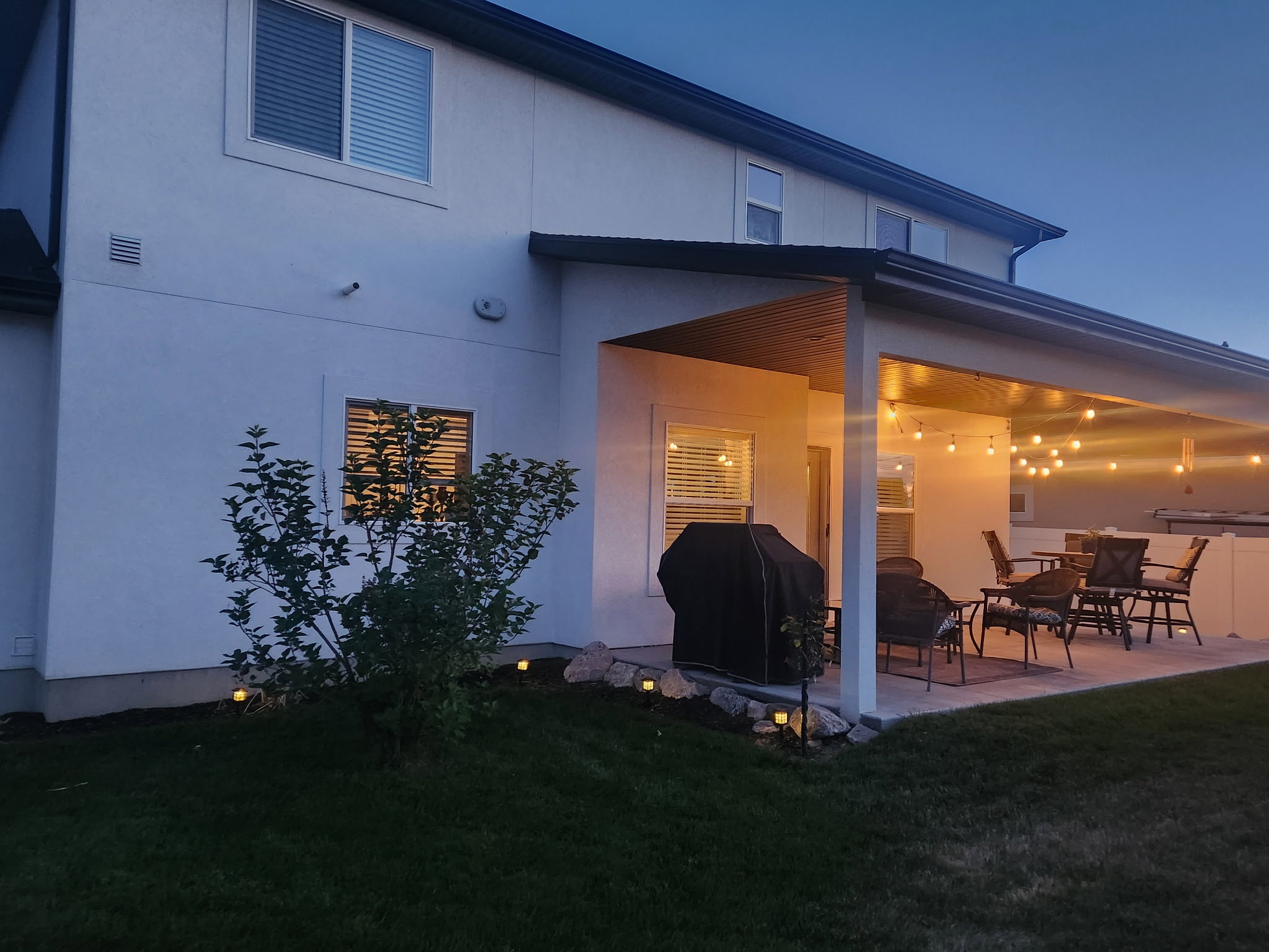 Covered patio featuring string lighting, a concrete surface, and a white privacy fence
