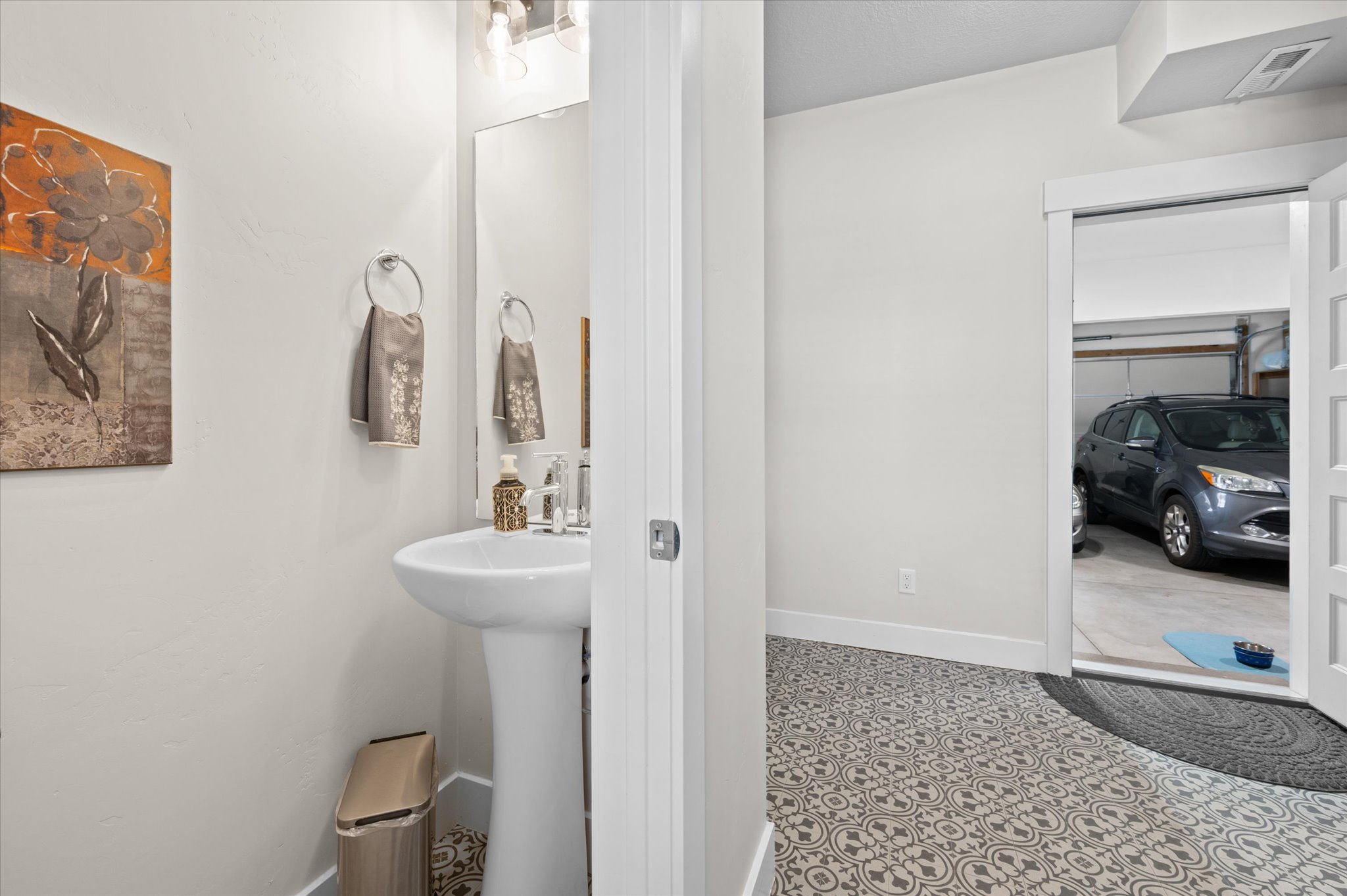 Pedestal sink with chrome faucet, illuminated by a vanity light fixture, set against light-toned walls