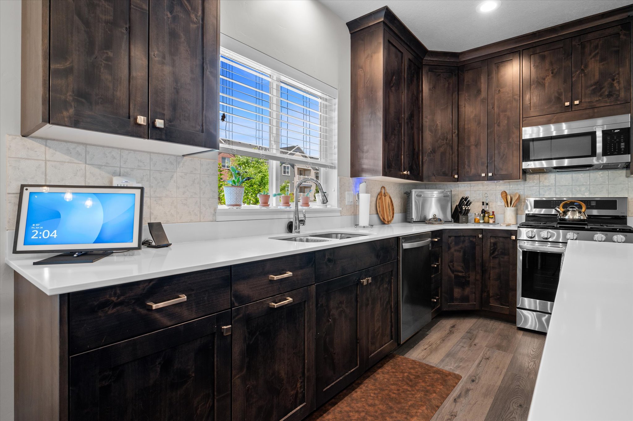 Kitchen featuring dark wood cabinetry, light-toned quartz  countertops, stainless steel appliances, and wood-finish flooring