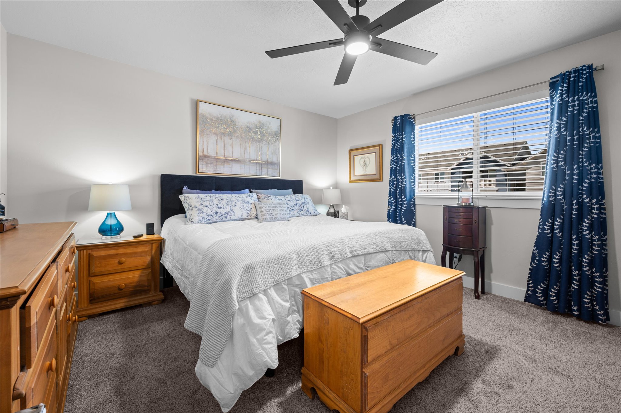 Carpeted bedroom featuring a large window, a ceiling fan with integrated lighting, and neutral wall tones