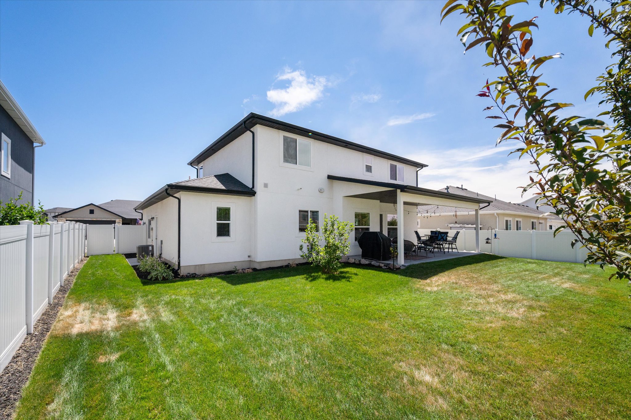 Expansive backyard featuring a manicured lawn, a full white privacy fence, and a covered patio for outdoor living