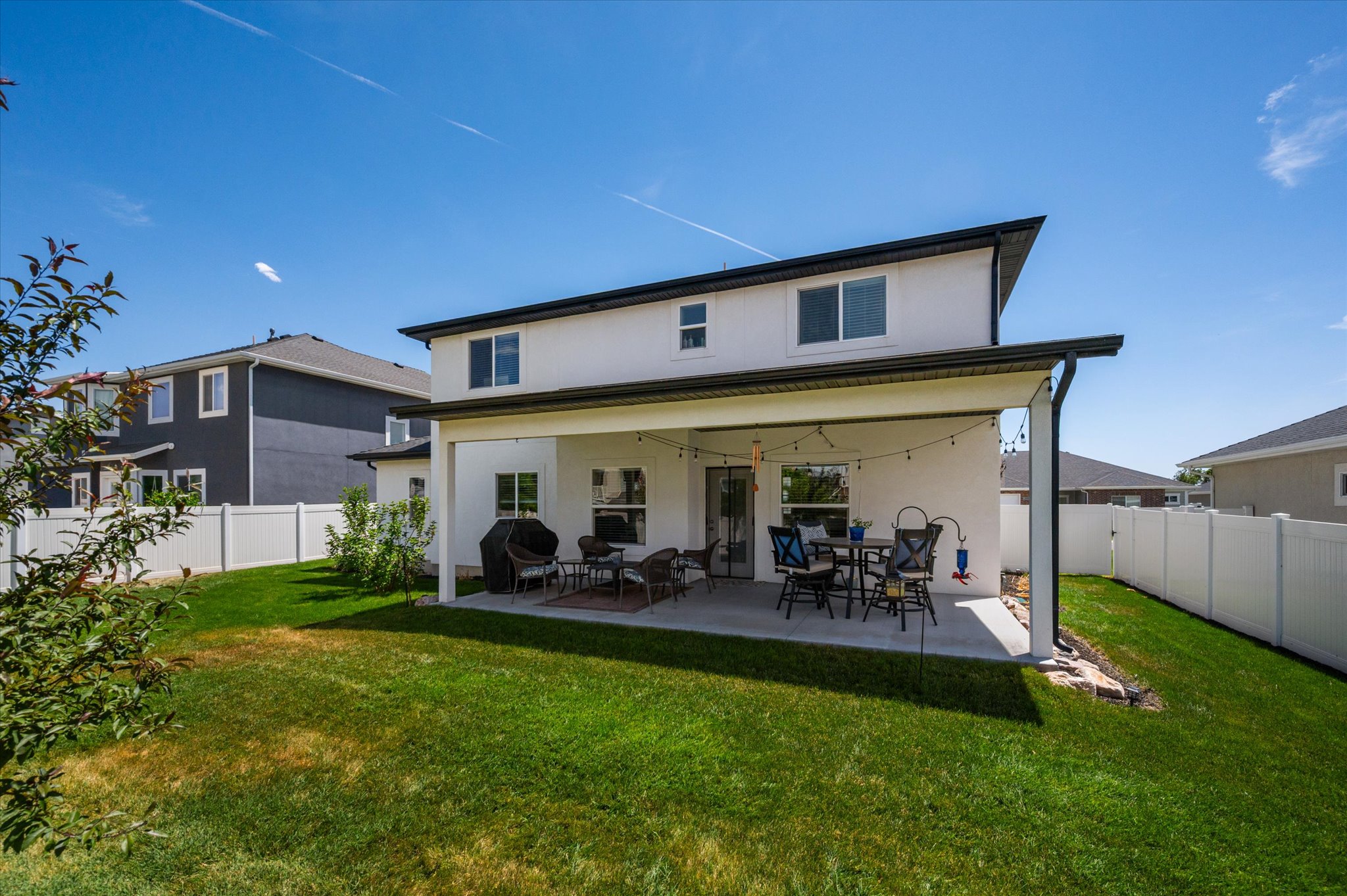 Rear exterior featuring a covered patio, expansive green lawn, and a white privacy fence