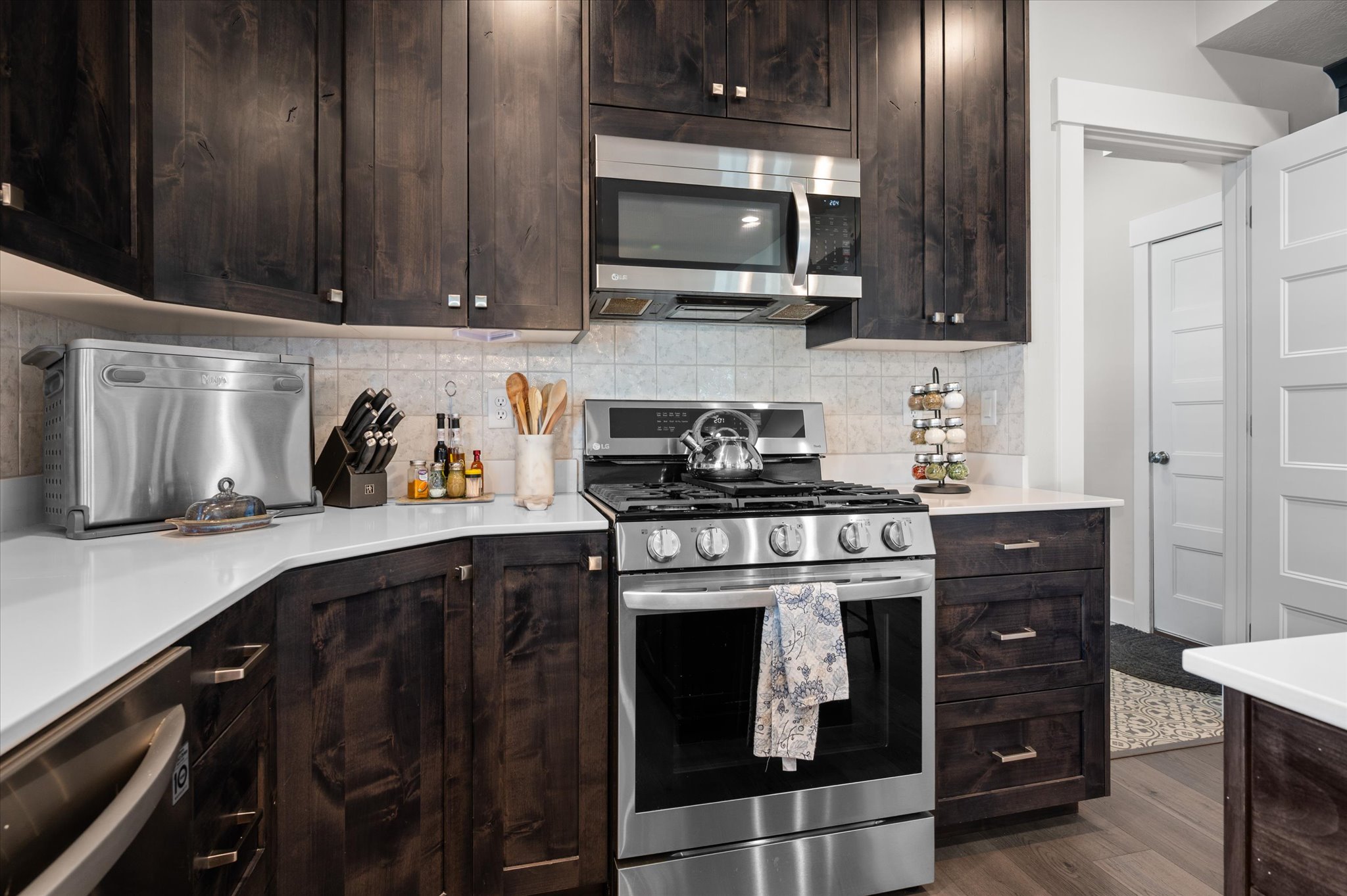 Modern kitchen featuring dark wood cabinetry, light quartz countertops, stainless steel appliances, a tile backsplash, and wood-finish flooring