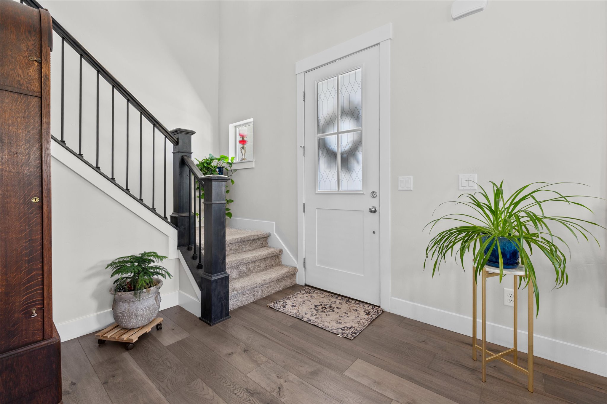 Entryway featuring wood-finish flooring, a white paneled door with a decorative glass insert, and a staircase with dark wood newel posts and black metal balusters
