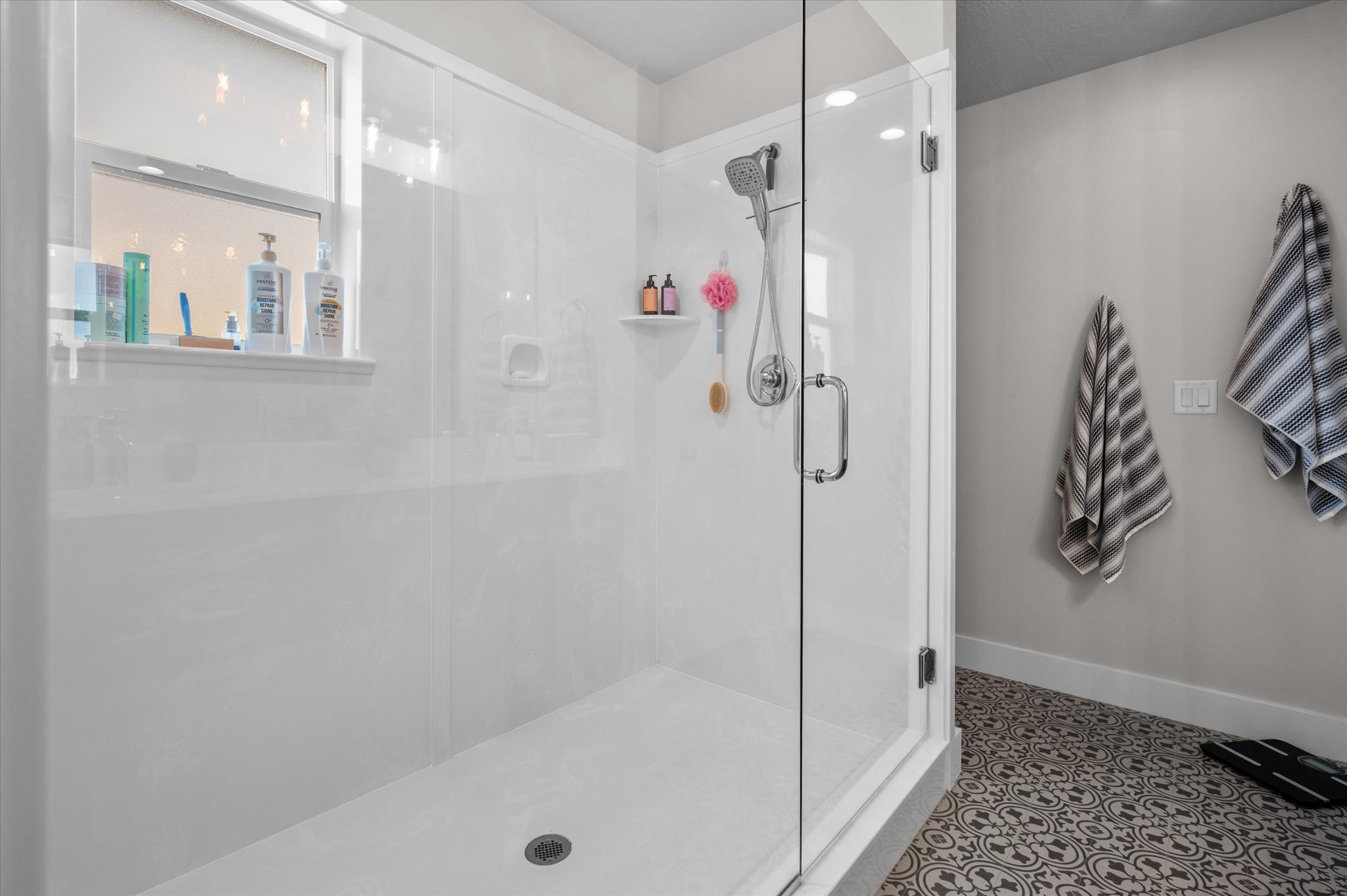 Primary owner bathroom with extra large Frameless glass shower enclosure featuring a white shower surround, chrome fixtures, and a functional window