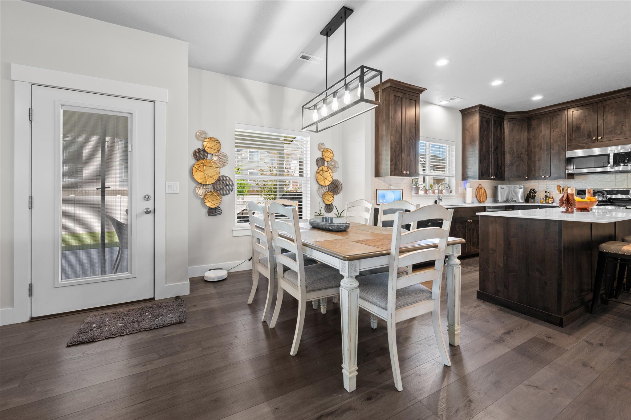 Open-concept dining area featuring wood-finish flooring, a contemporary linear chandelier, and a glass-paneled exterior door