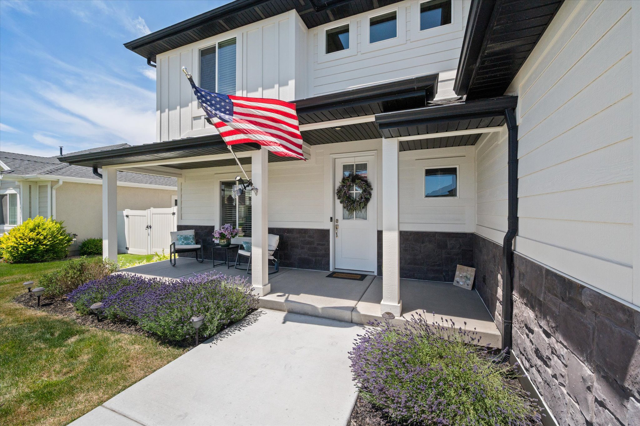 Inviting covered front porch with white columns, dark stone veneer siding, white horizontal siding, dark fascia, and concrete walkway