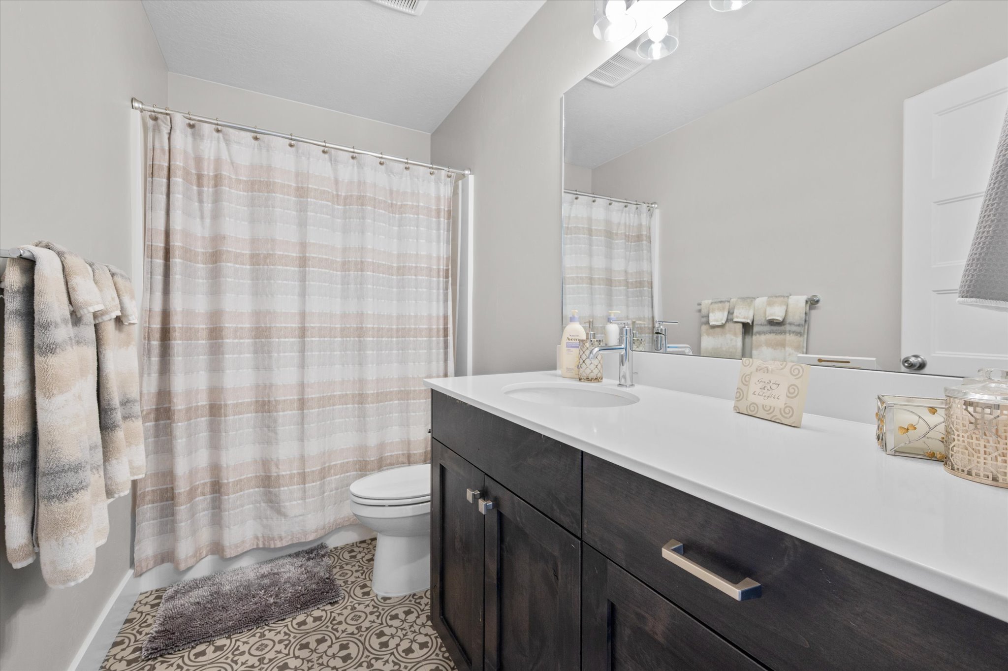 Bathroom featuring a dark wood-finish vanity with a white countertop and integrated sink, a large mirror, a toilet, and patterned floor