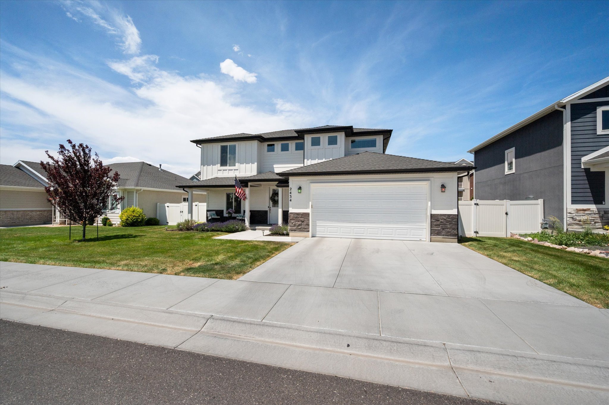 Contemporary two-story residence featuring a two-car garage, concrete driveway, stone accents, and a covered porch