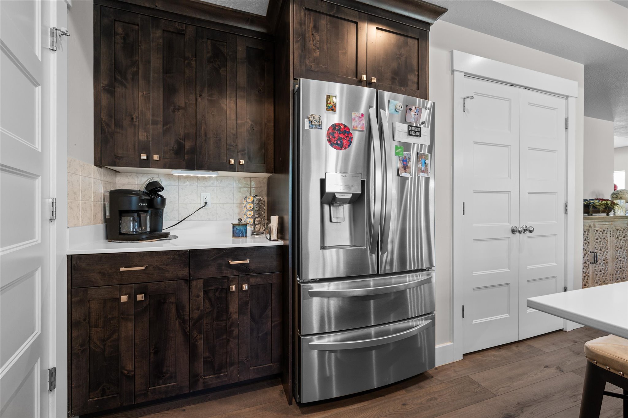 Kitchen area featuring dark wood-finish cabinetry, a stainless steel refrigerator, white quartz countertops, and a neutral tile backsplash