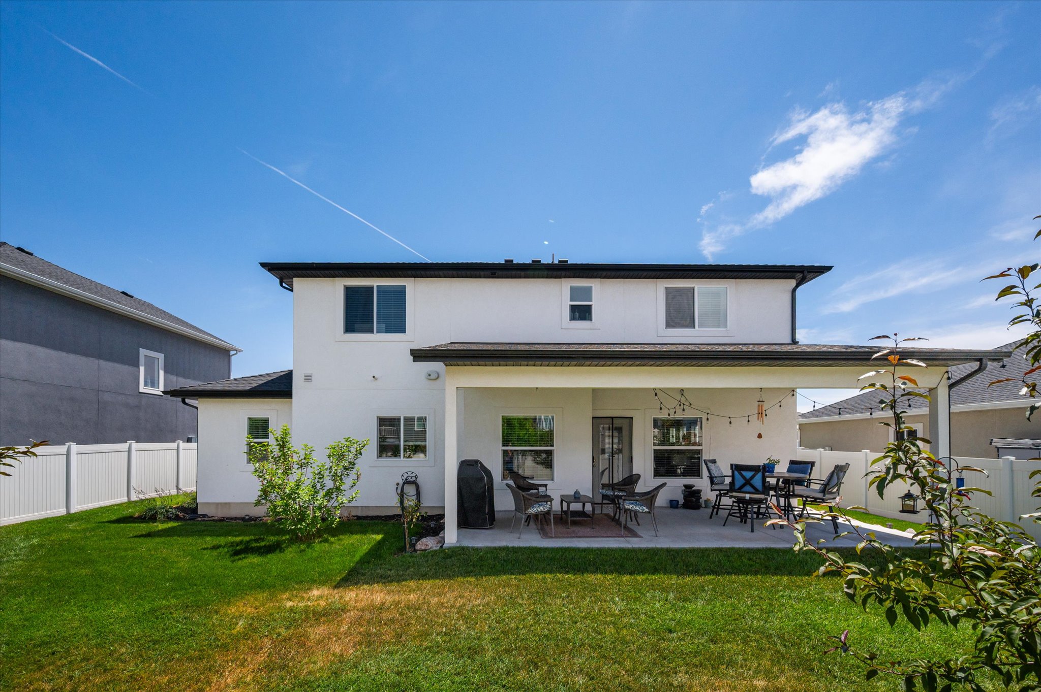 Expansive backyard featuring a covered concrete patio, manicured lawn, and white vinyl perimeter fencing