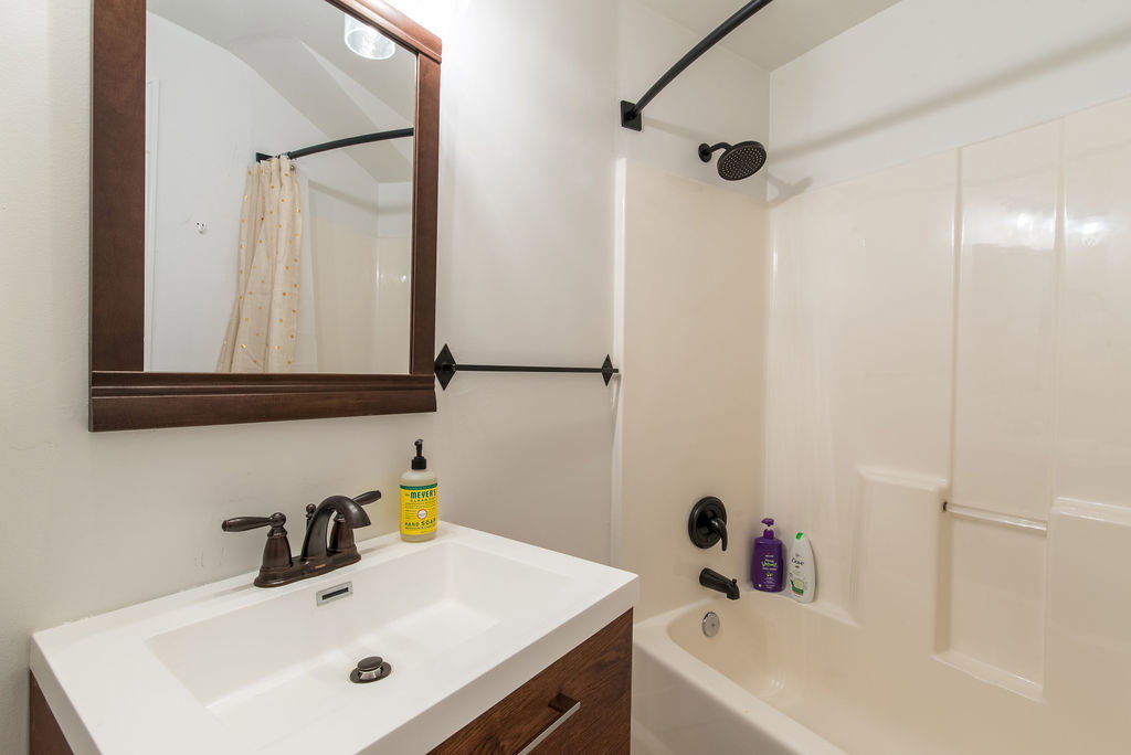 Bathroom featuring a white integrated sink vanity with a wood-finish cabinet, dark bronze hardware, and a framed mirror