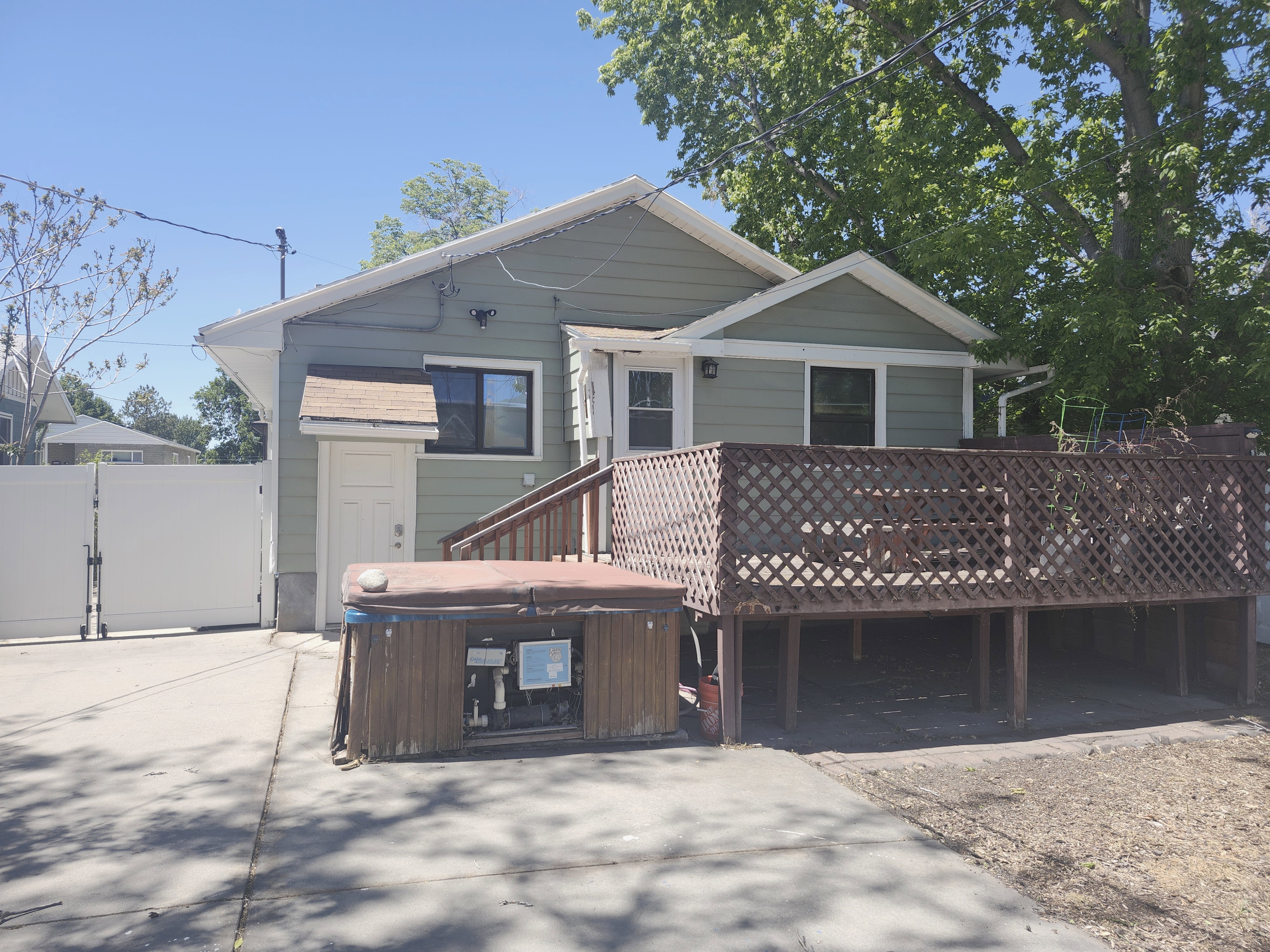 Rear exterior featuring a spacious elevated wood deck with lattice railing, an adjoining concrete patio, a private side entrance, and a white vinyl fence