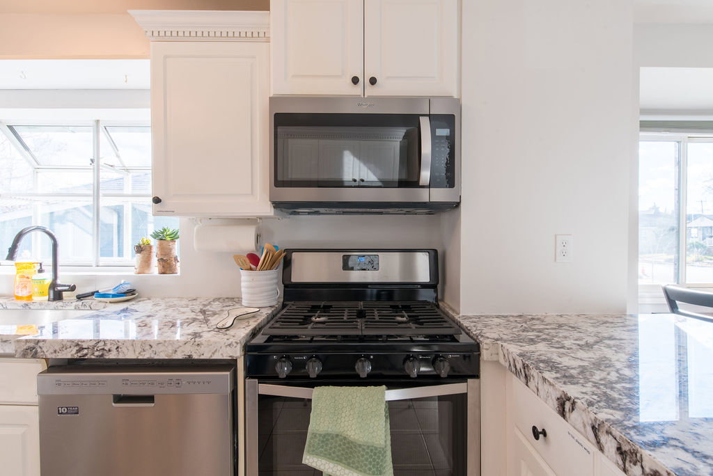 Kitchen featuring white cabinetry with black hardware, mottled countertop, stainless steel over-the-range microwave, stainless steel range, and stainless steel dishwasher