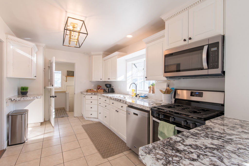 Bright kitchen featuring white cabinetry with dark hardware, granite-patterned countertops, stainless steel appliances, and a tiled floor