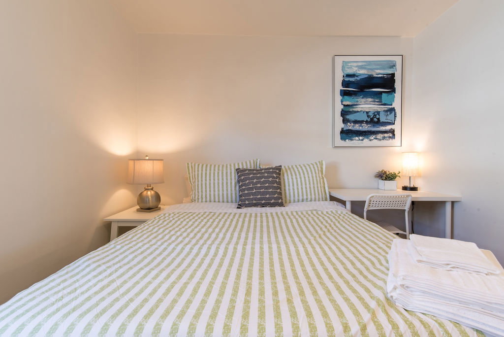 Bedroom featuring light-toned walls, a white side table, and a white desk with a coordinating chair