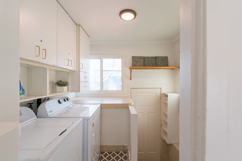 Dedicated utility room with ample white cabinetry featuring gold-toned hardware, a window for natural light, and countertop space
