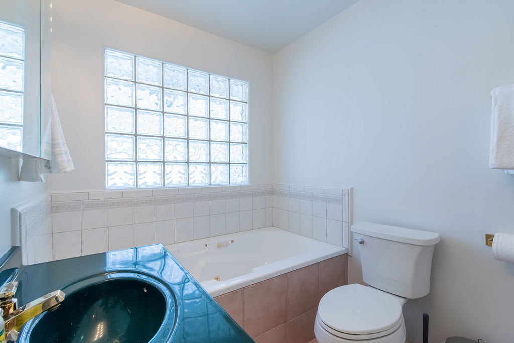 Bathroom featuring a glass block window, jetted tub, ceramic tile surround, integrated sink, and white toilet