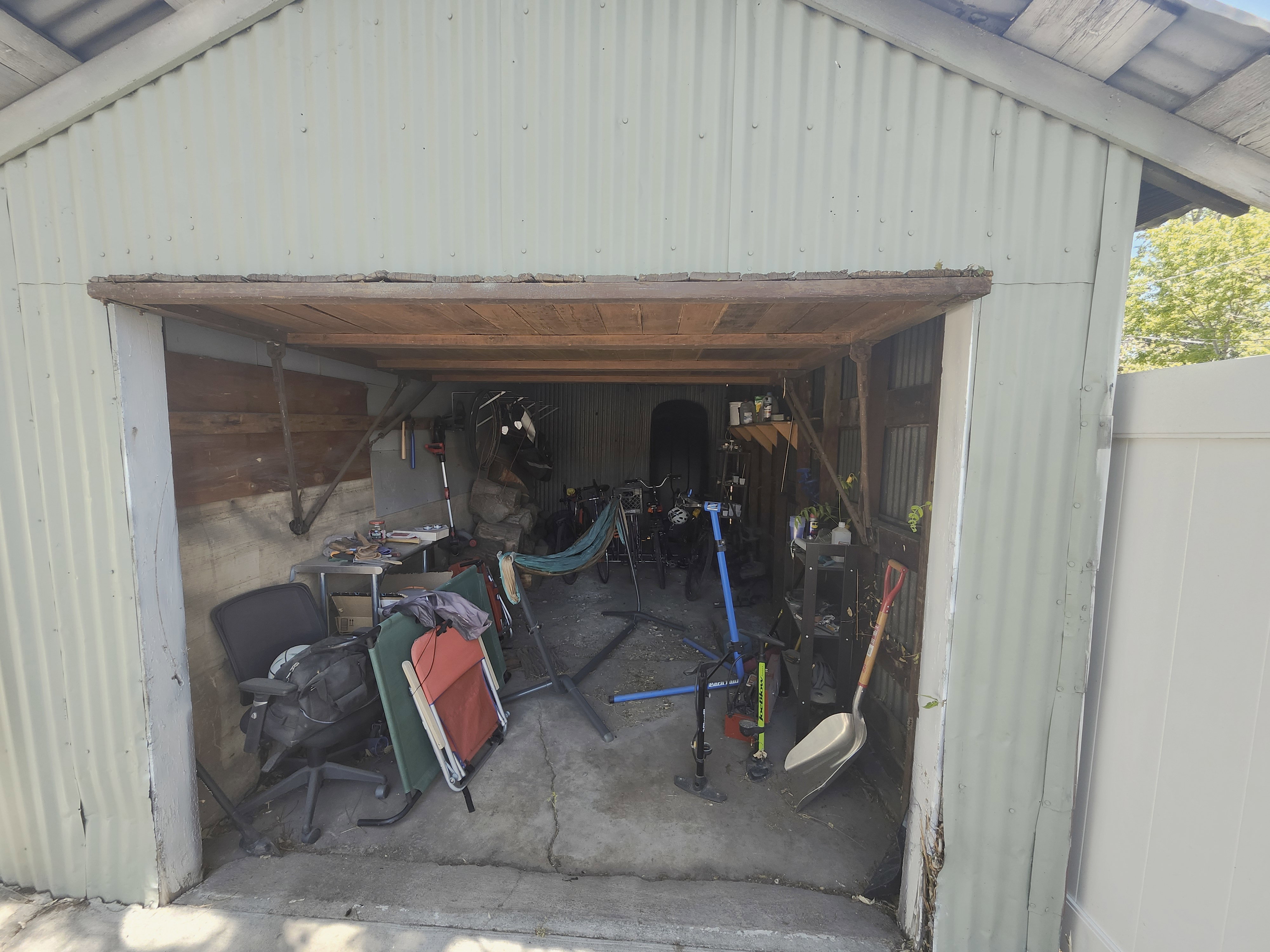 Detached corrugated metal structure with a wood-lined entry, concrete flooring, and an adjacent vinyl fence