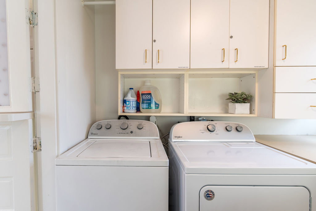 Dedicated laundry space featuring white cabinetry with gold-tone hardware, open shelving, and a light-toned countertop