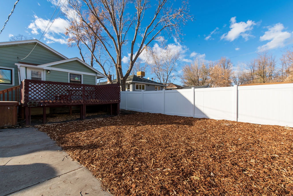Spacious backyard with a large wooden deck, white privacy fencing, and wood chip ground cover