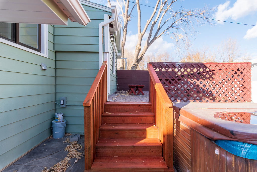 Wood-stained outdoor staircase leading to a brick patio, featuring a lattice privacy screen and a built-in spa