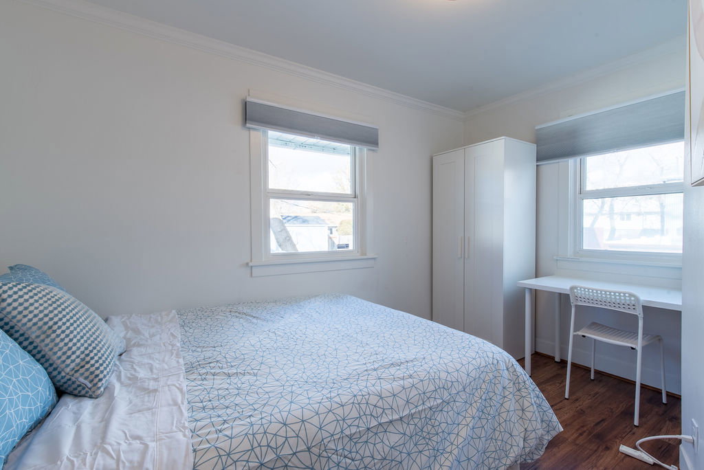 Bright room featuring two windows with roller shades, white trim, and wood-finish flooring
