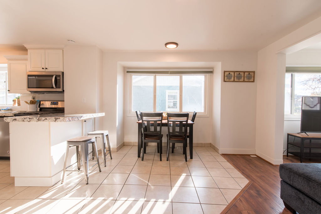 Kitchen and dining area featuring a breakfast bar with stone-finish countertop, white cabinetry with silver-tone hardware, stainless steel appliances, and tile flooring