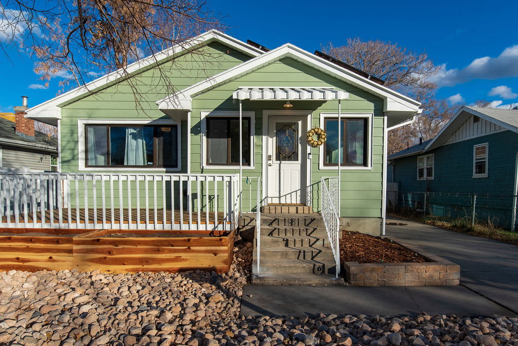 Green siding exterior featuring a front deck with white railing, concrete steps with metal railing, a covered entryway, and a rock landscaping bed