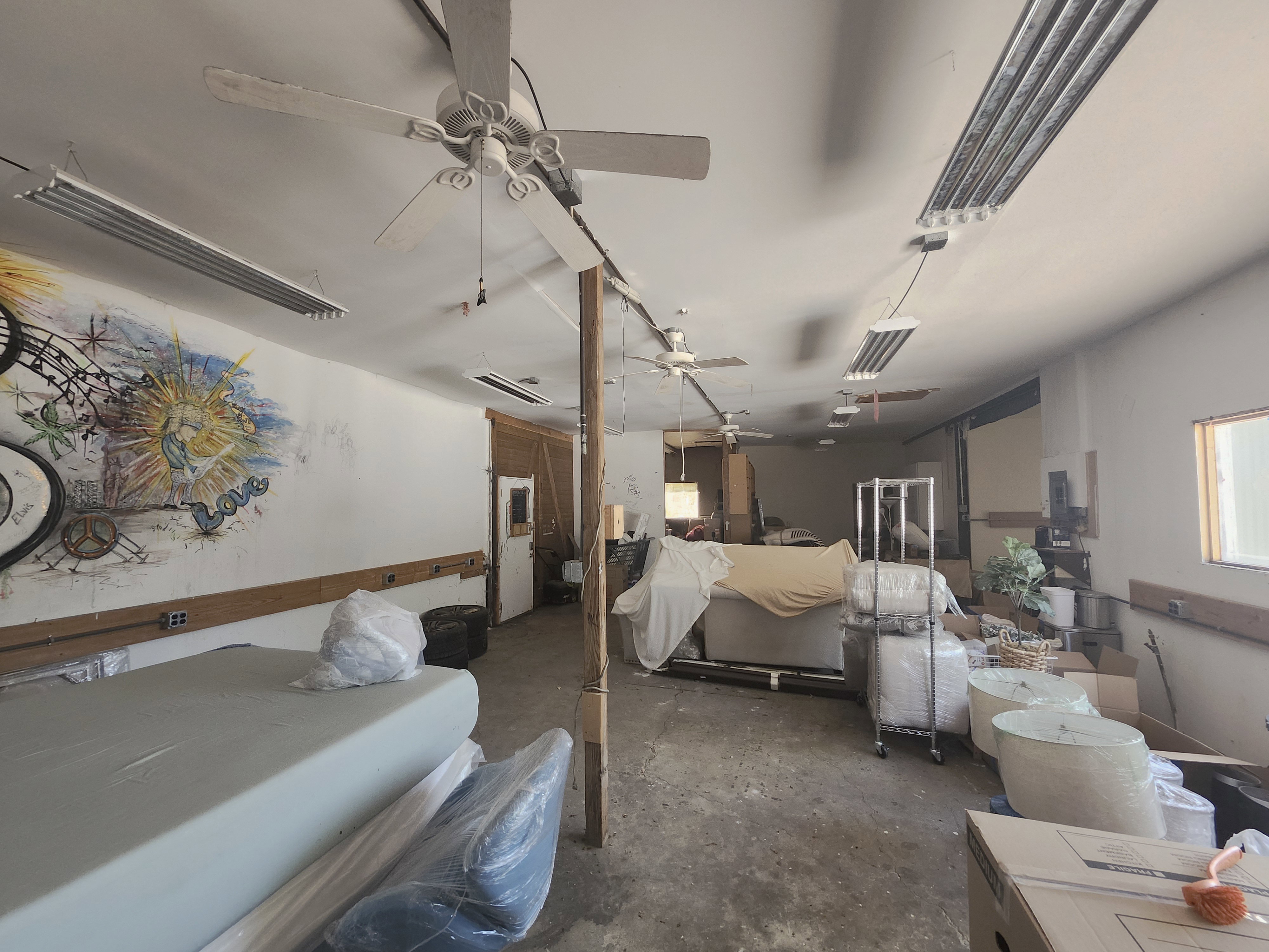 Spacious interior featuring a high ceiling, multiple ceiling fans, and fluorescent lighting