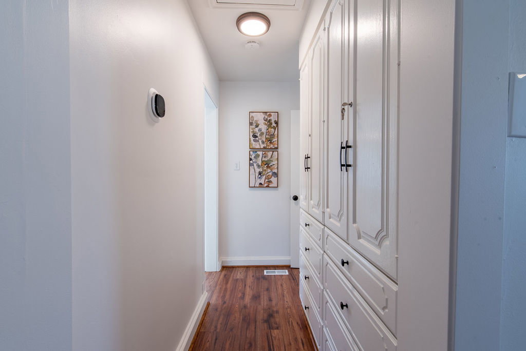 Hallway with wood-finish flooring, recessed ceiling light, and built-in white cabinetry featuring black hardware