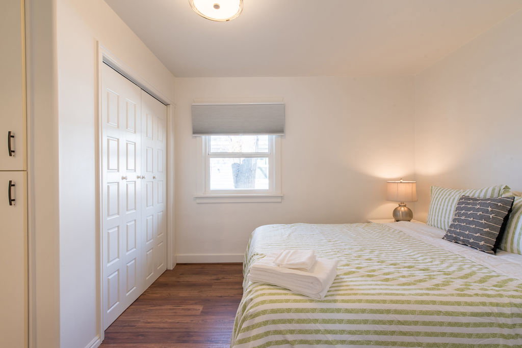 Bedroom featuring wood-finish flooring, a double-panel bi-fold closet, a single window with a gray roller shade, and a flush-mount ceiling light