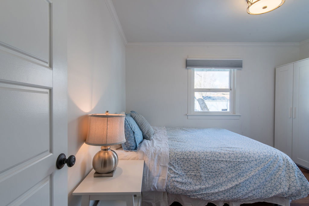 Bedroom featuring a paneled interior door with dark hardware, crown molding, a window with a roller shade, and a built-in wardrobe