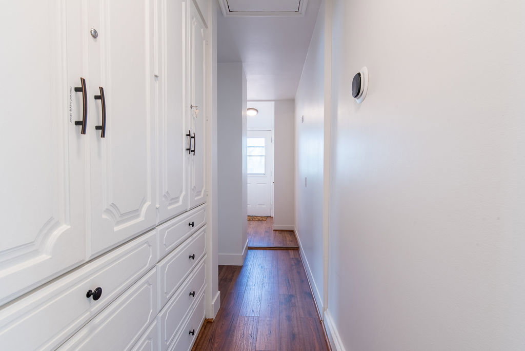 Hallway featuring wood-finish flooring, white built-in cabinetry with panel detailing, black hardware, and a modern wall-mounted thermostat