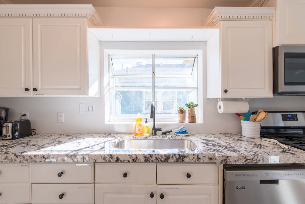 Kitchen featuring white shaker-style cabinetry with dark hardware, a stainless steel sink with a dark faucet, and light-toned countertops with dark veining