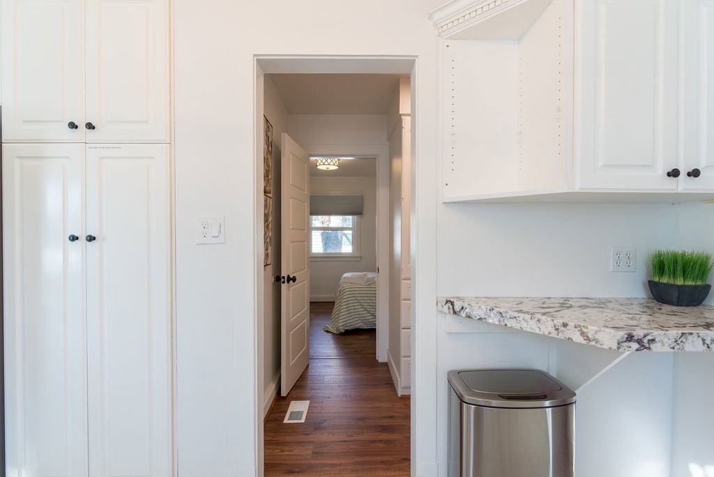 White cabinetry with black hardware, stone-finish countertops, and wood-finish flooring visible through the doorway