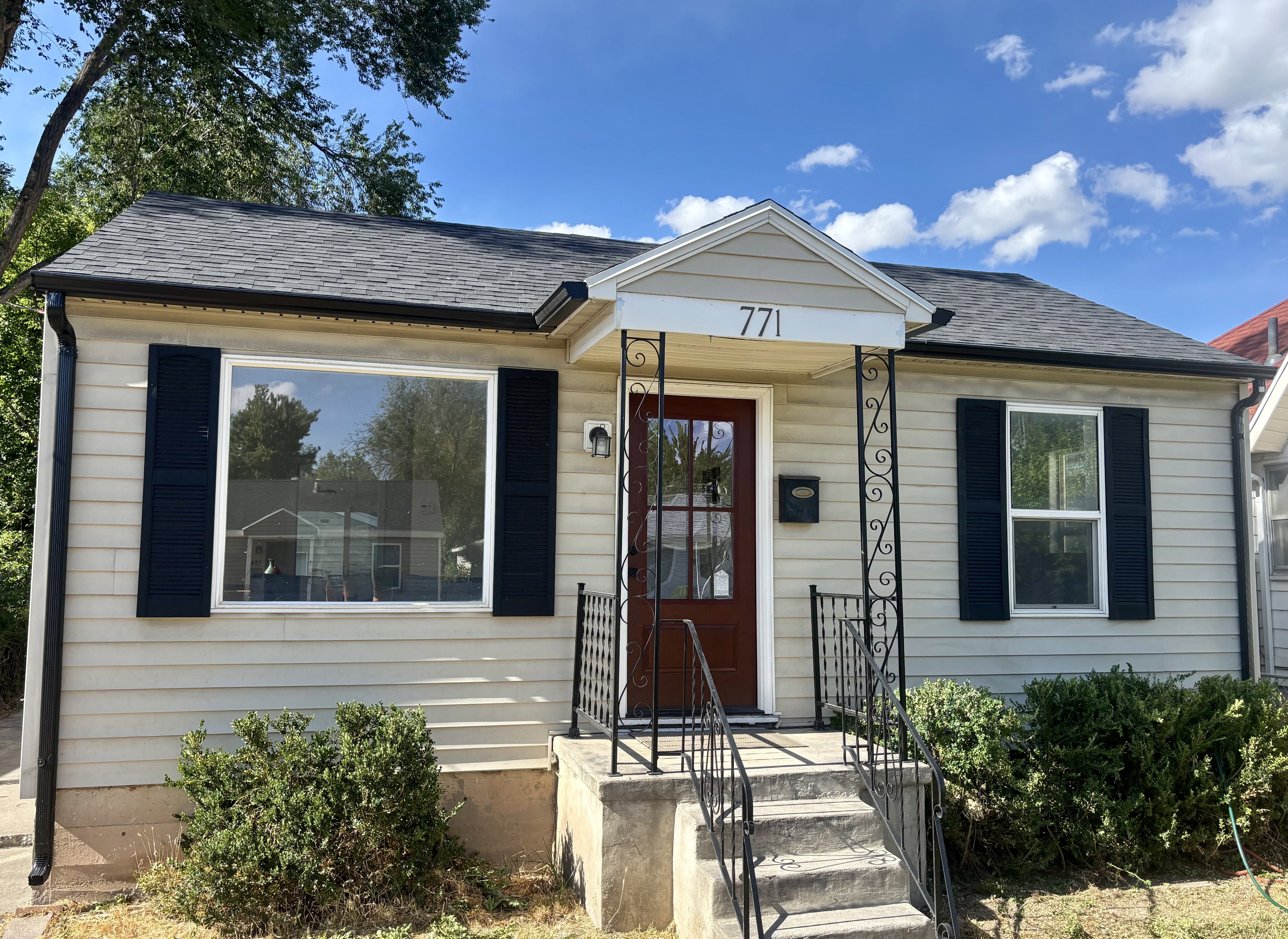 Front exterior featuring light-colored siding, dark shutters, and a dark asphalt shingle roof