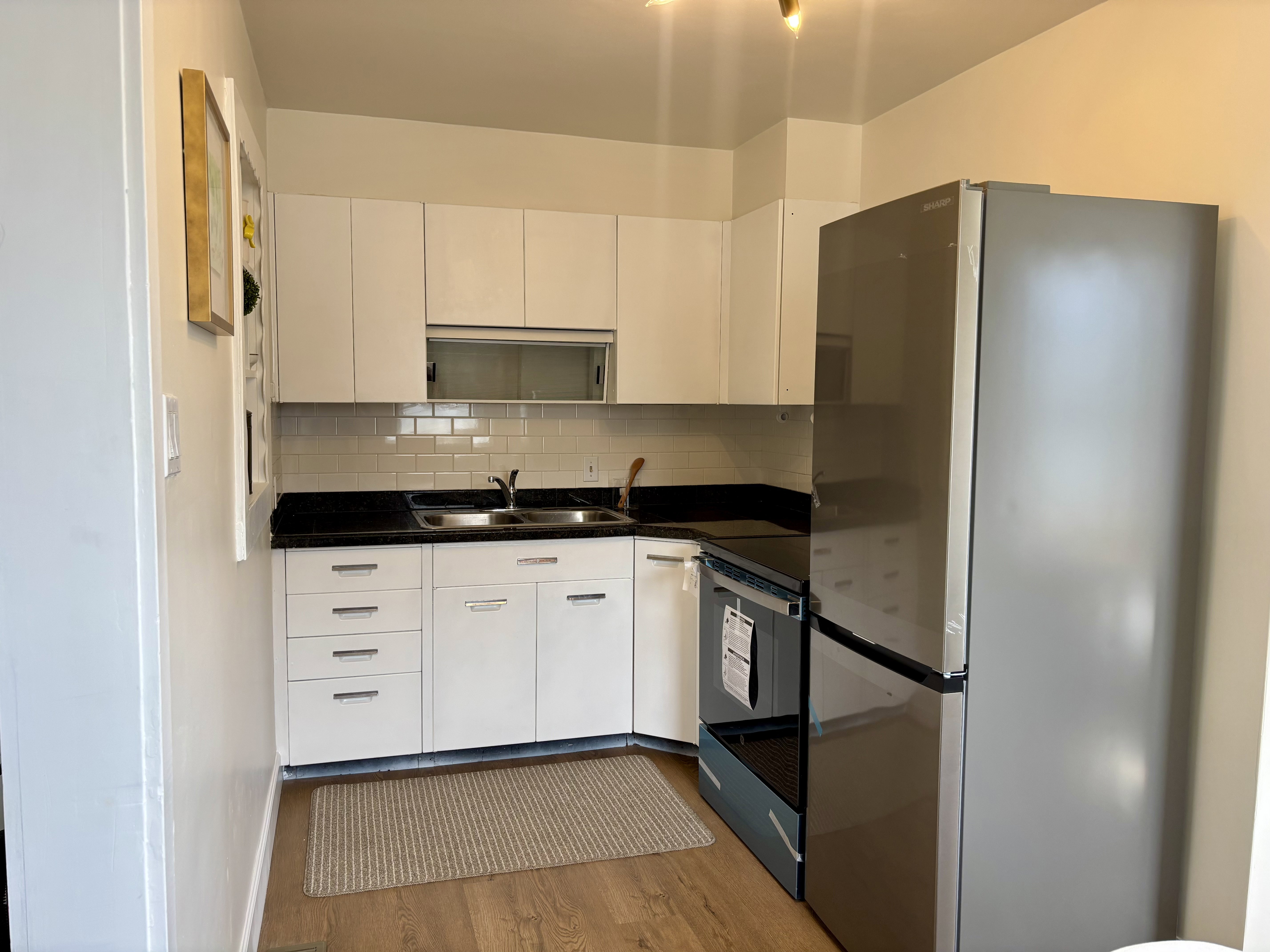 Compact kitchen featuring white cabinetry, dark countertops, a stainless steel refrigerator, a black range, and wood-finish flooring