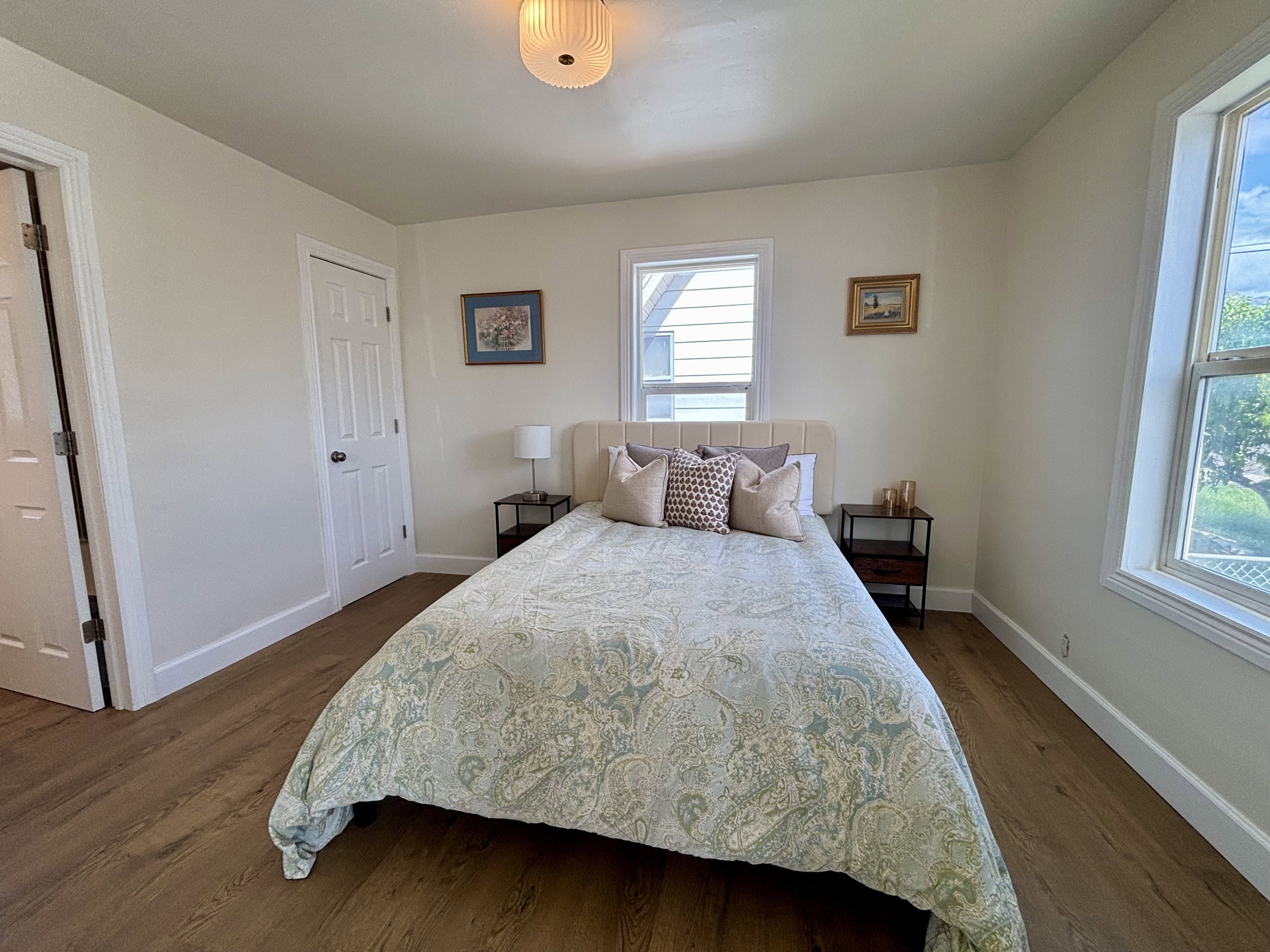 Room featuring wood-finish flooring, two windows with white trim, a ceiling-mounted light fixture, and a paneled door