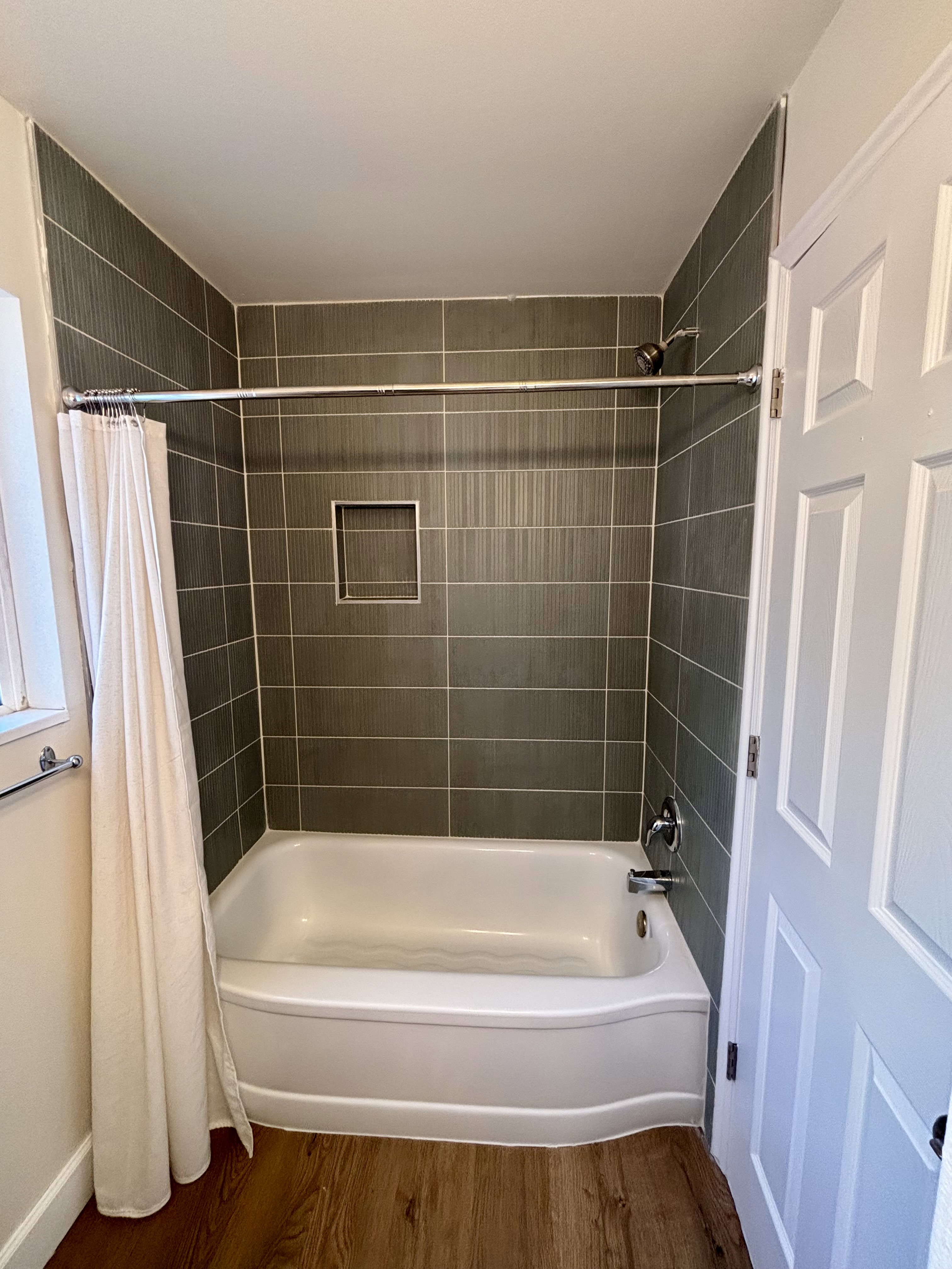 Bathroom featuring a tiled tub surround with a recessed niche, showerhead, and a white bathtub