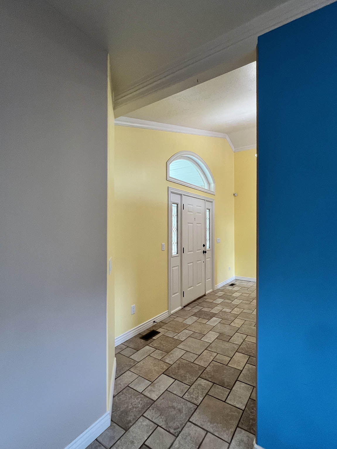 Entryway featuring varied-size floor tiles, a white paneled door with sidelights, and an arched transom window