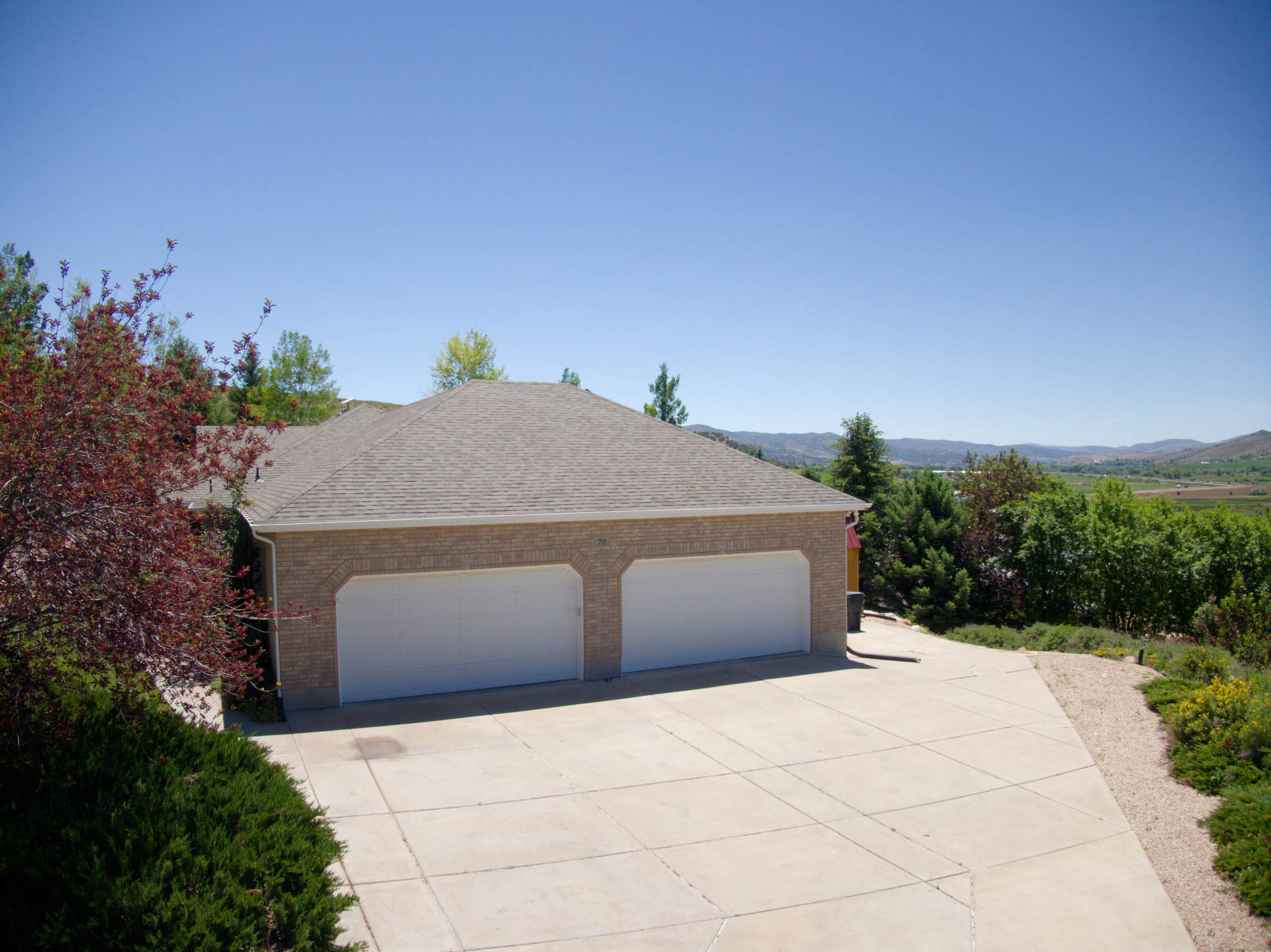 Brick exterior featuring two garage doors, a concrete driveway, and mature landscaping
