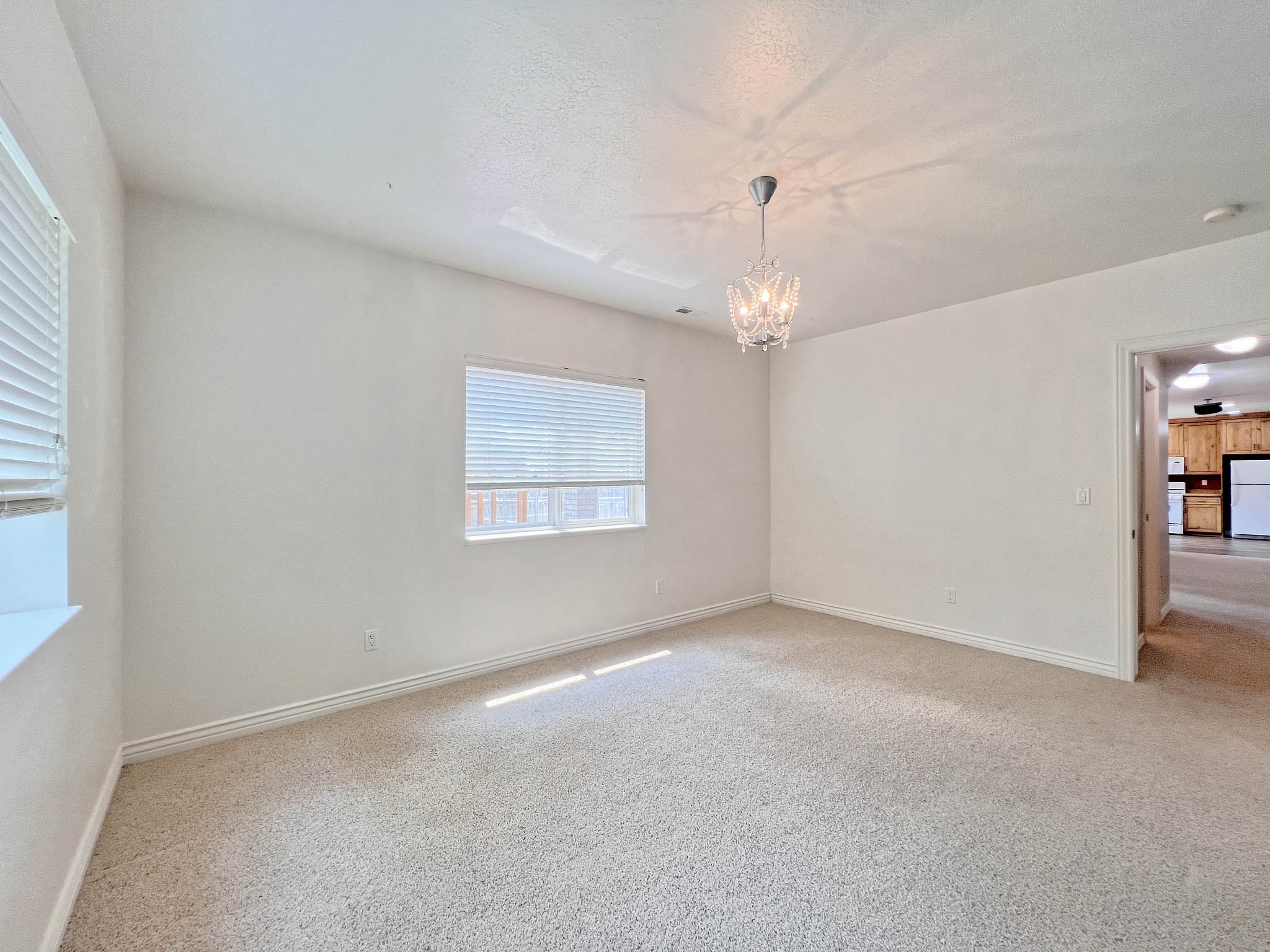 Carpeted interior space featuring a crystal chandelier, two windows with blinds, and white baseboards