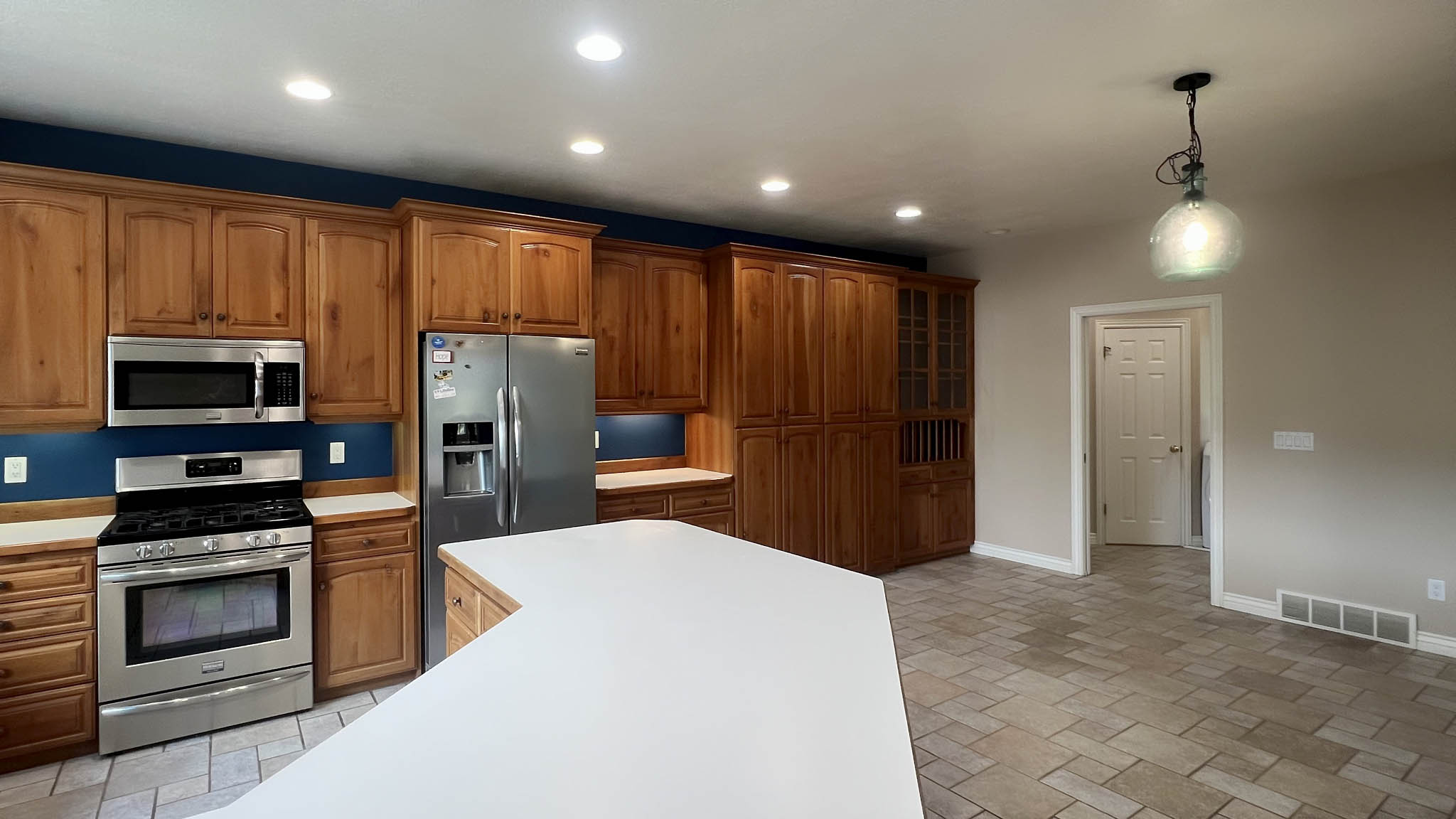 Kitchen featuring abundant wood cabinetry, stainless steel appliances, a large central island with white countertops, recessed lighting, and tile flooring
