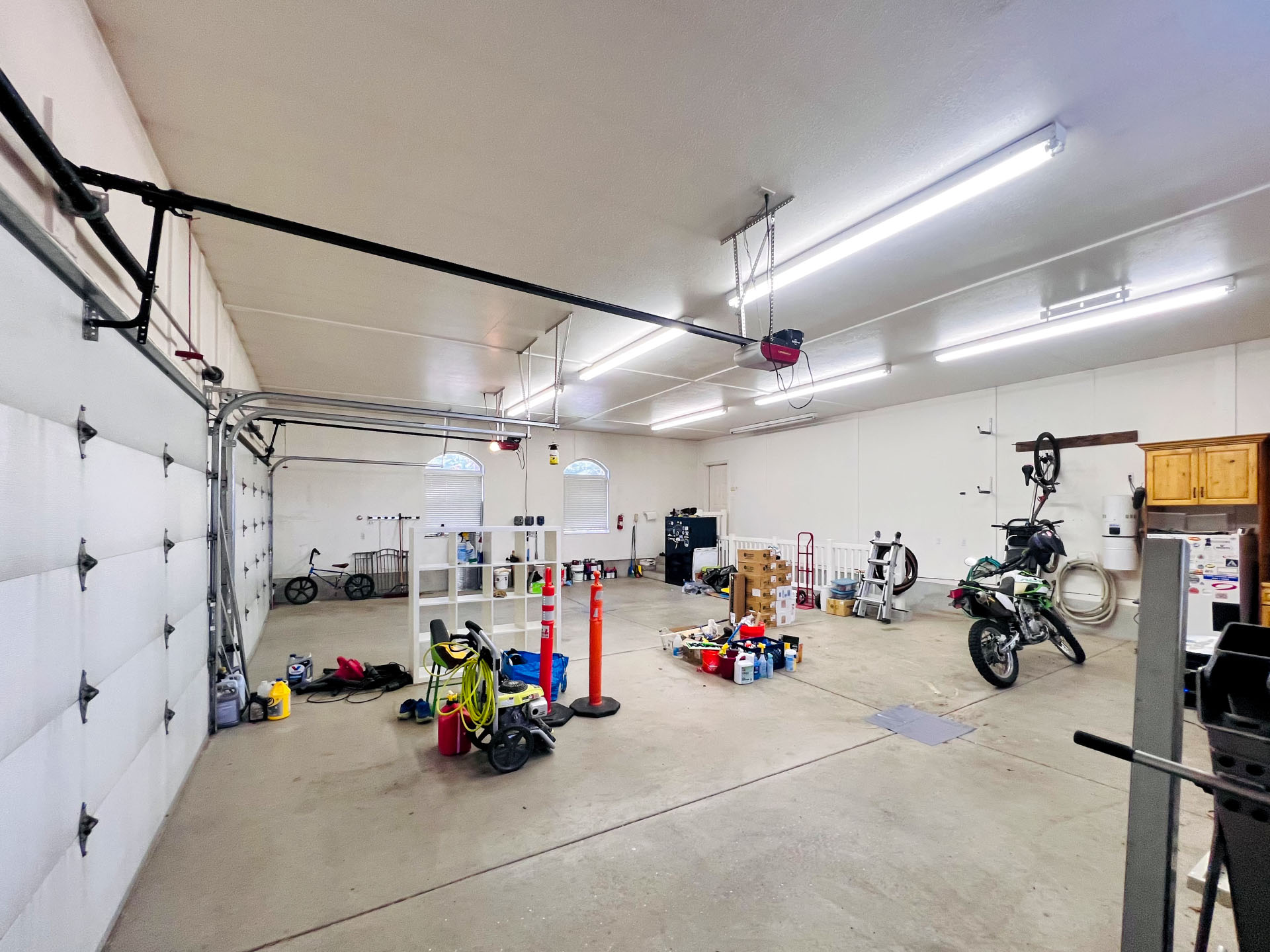 Spacious garage with multiple fluorescent light fixtures, a light-colored concrete floor, and white walls