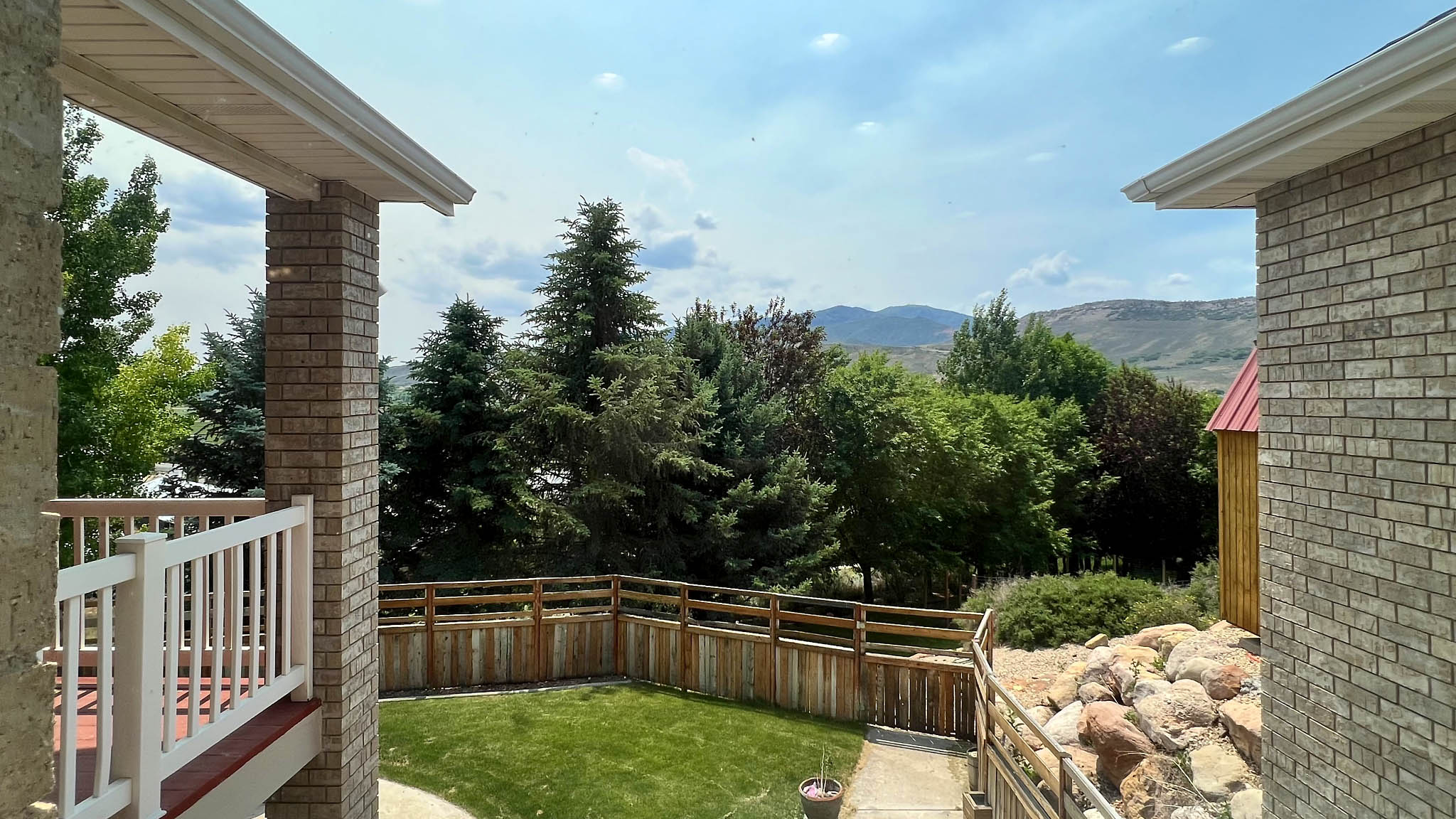 Brick exterior detailing, white railing, and a fenced yard with mature trees