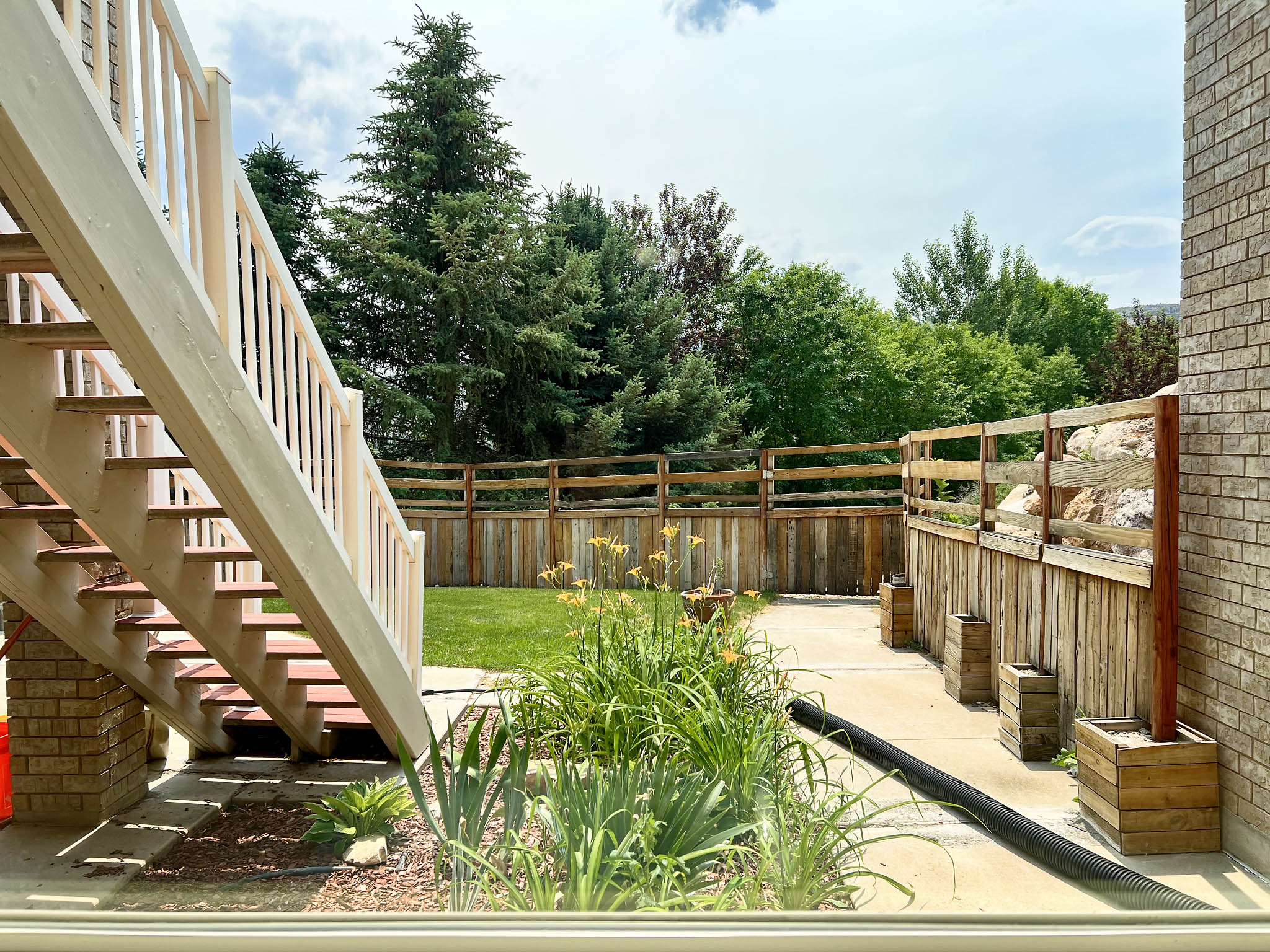 Outdoor wooden staircase with painted white railings descending to a concrete patio