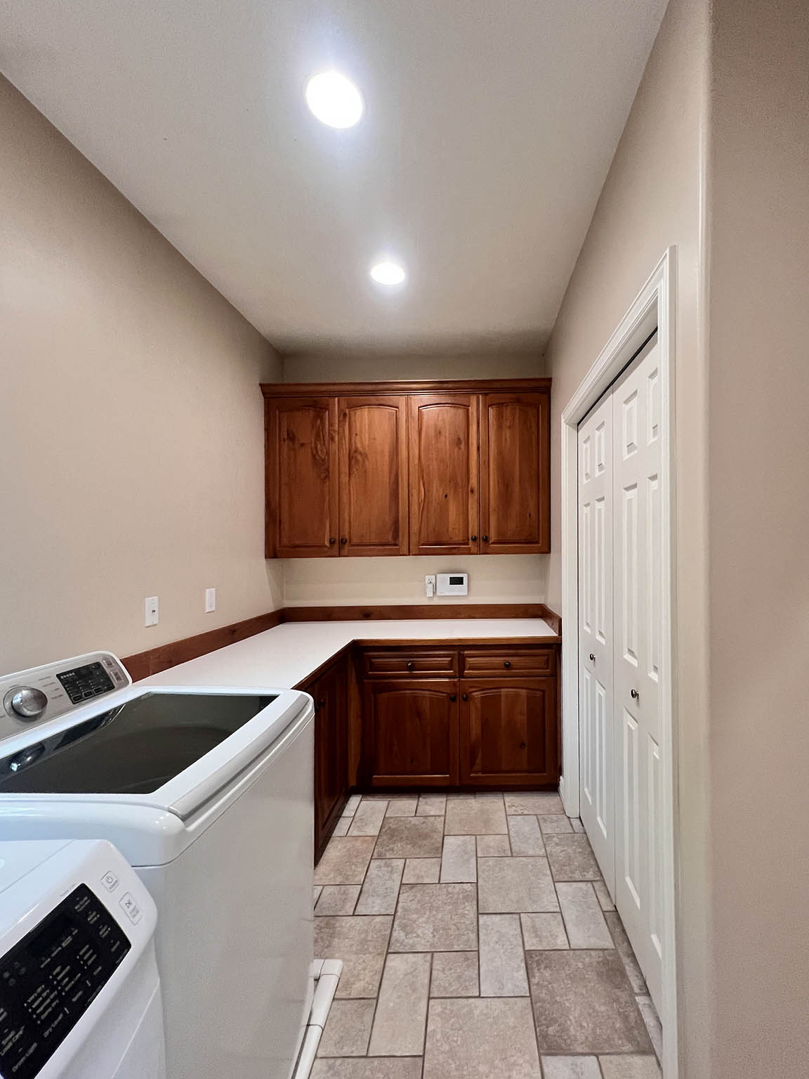Utility area featuring recessed lighting, a full wall of wood-finish cabinetry, extensive countertop space, and patterned tile flooring