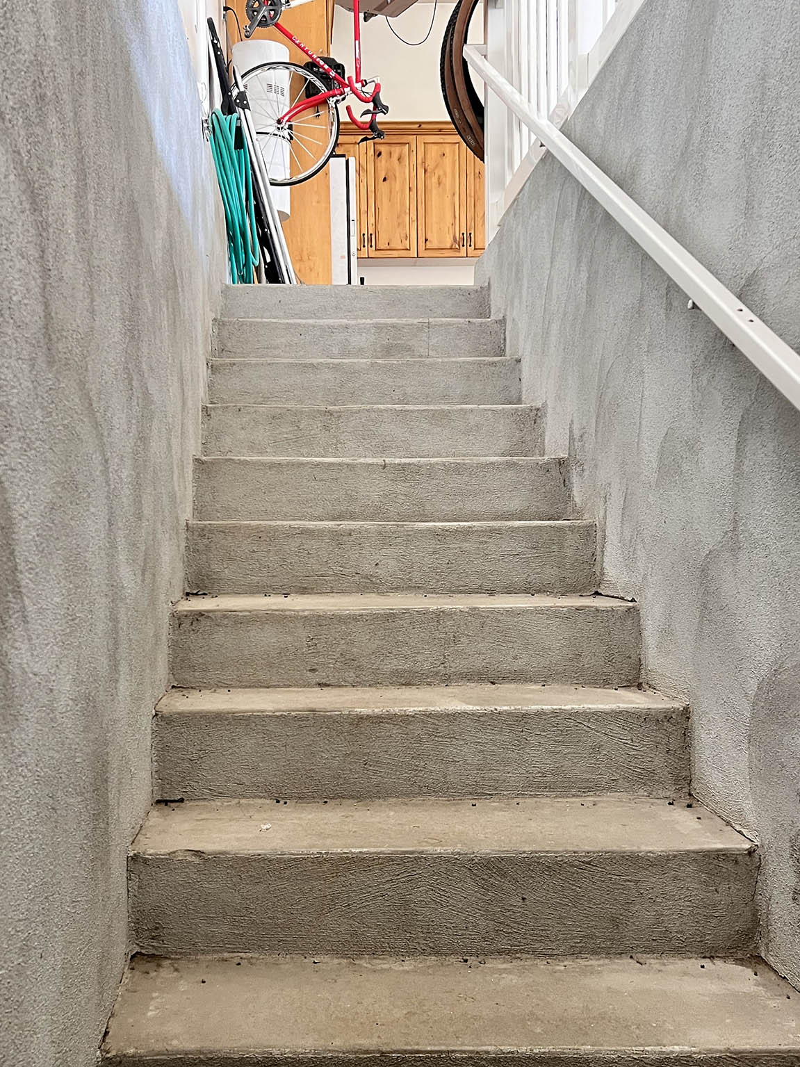 Concrete staircase with textured wall finishes and a white handrail leading to an upper landing with built-in wood cabinetry